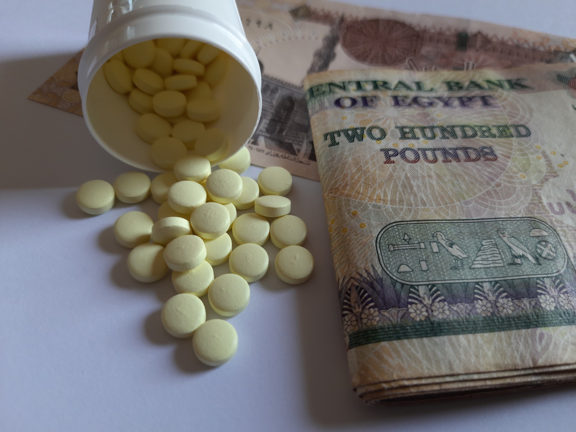 Aspirin tablets in a white plastic box on a white background, egyptian with Egyptian currency notes of 200 pounds, health economics, pharmaceutical economics